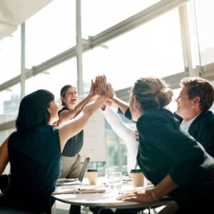 Business team celebrating success with a group high-five in a modern office setting.