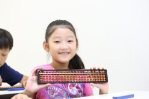 Smiling girl holding an abacus in classroom during maths learning session.