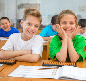 Two smiling children sitting at school desks with abacus tools in a classroom.