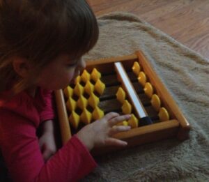 Young child learning maths using a wooden abacus at home.